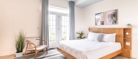 Un dormitorio moderno con una cama grande, cabecera de madera, una silla, una planta en maceta y vistas al exterior a través de una puerta de cristal.