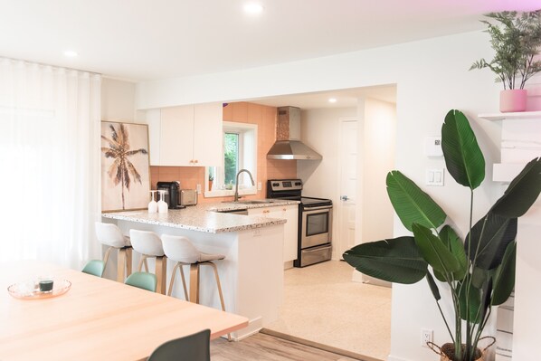 Una cocina moderna con armarios blancos, una isla central con taburetes de bar, electrodomésticos de acero inoxidable y una planta verde grande.