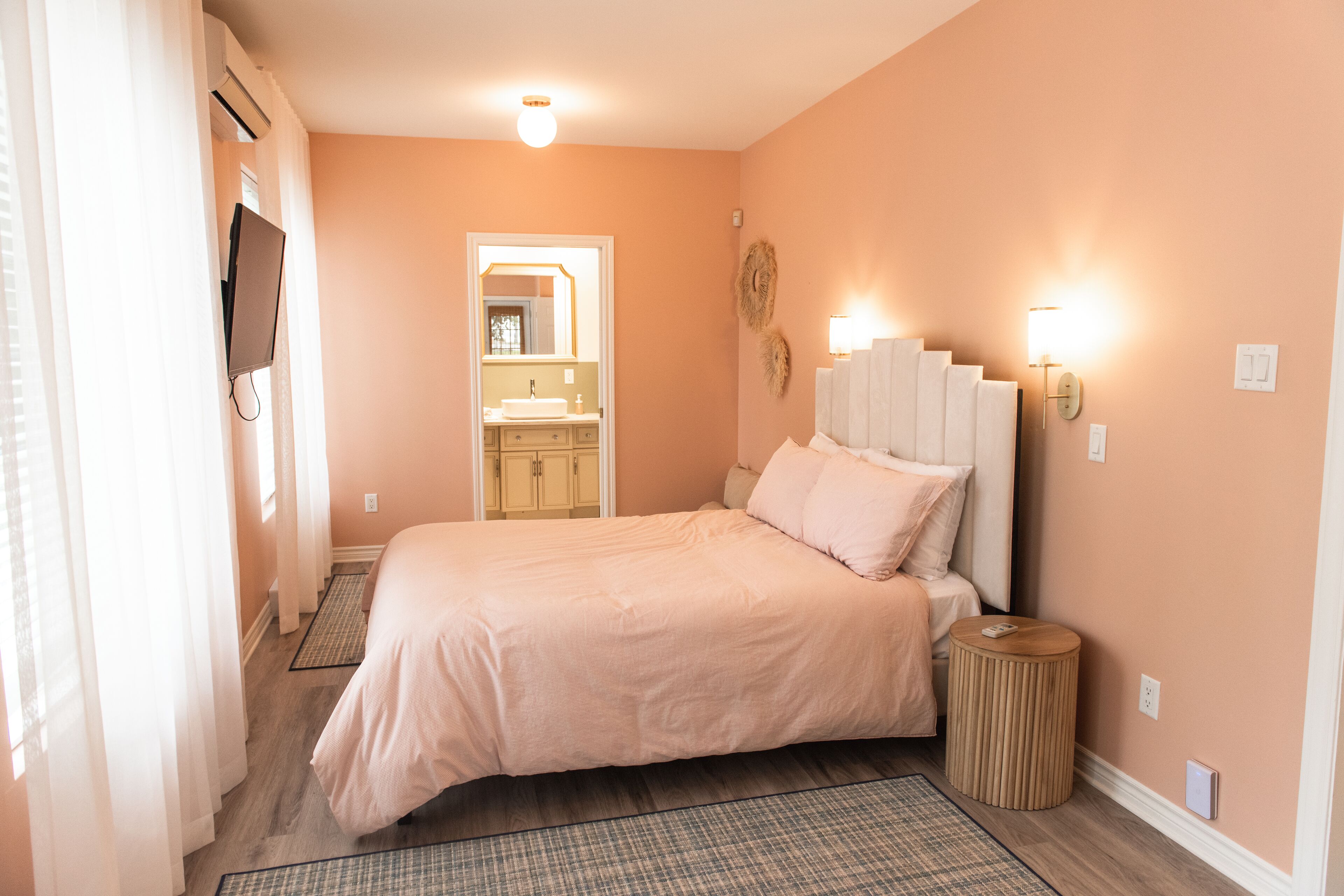 A bedroom with a bed, bedside lamps, a mirror, and a bathroom visible through an open door.