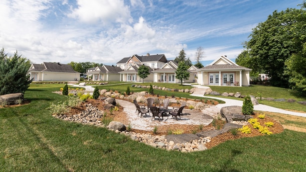 A residential area with a well-maintained lawn, a patio with outdoor furniture, and a row of houses with similar architectural styles. - Hôtel Le Rosay (Venise-en-Quebec)