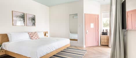 A modern bedroom with a wooden bed, a striped rug, and a pink door leading to a bathroom.