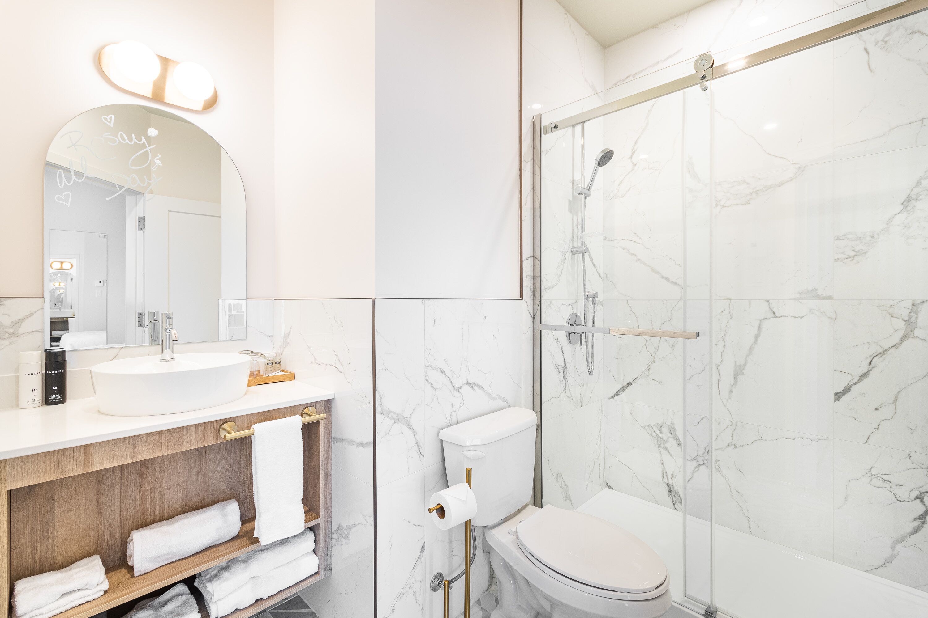 Une salle de bain moderne avec un mur en marbre, un grand miroir, un lavabo, des toilettes et une douche à parois de verre.