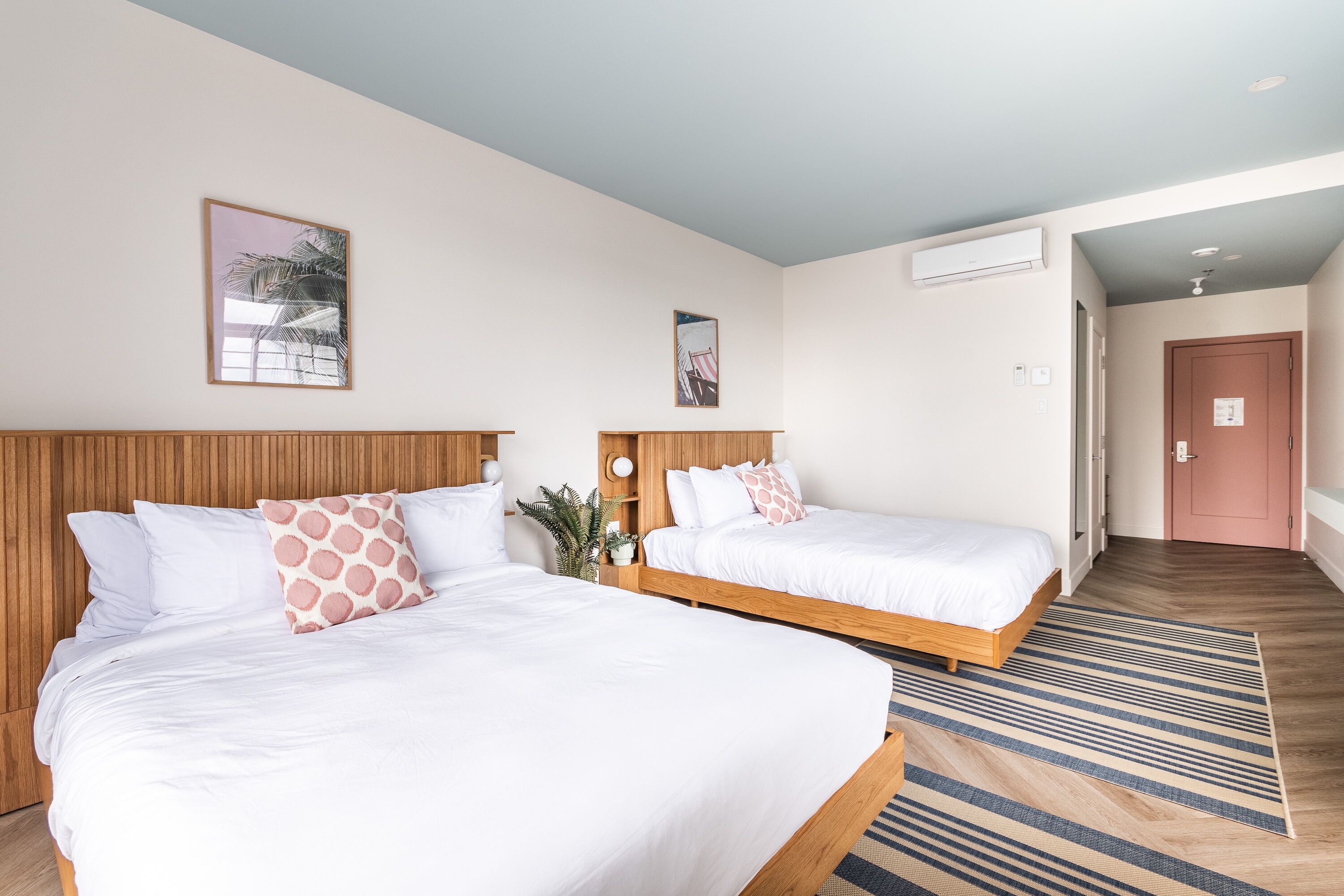 Habitación de hotel con dos camas, cabecero de madera, alfombra a rayas y una puerta que da a otra habitación.