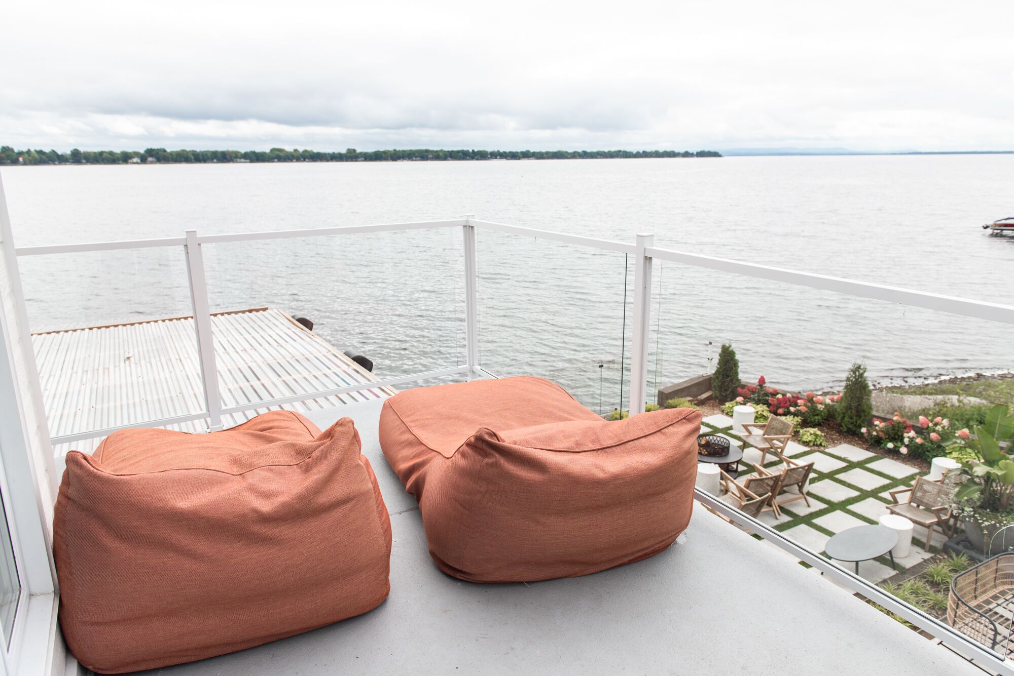 Ein Balkon mit zwei orangenen Sitzsäcken, einer weißen Brüstung und Blick auf ein ruhiges Gewässer.
