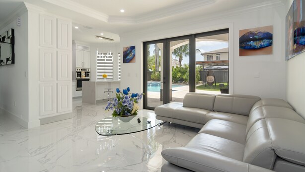 A modern living room with a marble floor, a glass coffee table, a beige leather sofa, and a view of a swimming pool through large glass doors. - Tropical Paradise deluxe villa (Miami)