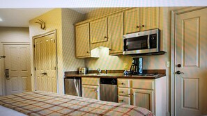 Cozy retreat with a compact kitchenette, featuring a bed with a checkered bedspread and a functional layout.