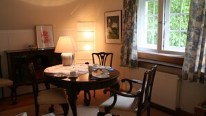 Une salle à manger avec une table ronde, des chaises, une lampe et une fenêtre avec des rideaux.