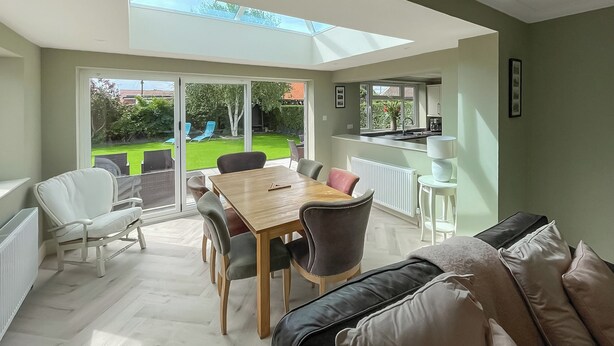 A bright room with a large table and chairs, a sofa, and a view of a garden through glass doors.