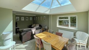 A dining area with a wooden table and chairs, a sofa, and a skylight above.