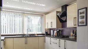 A modern kitchen with white cabinets, a black countertop, and a window with blinds.