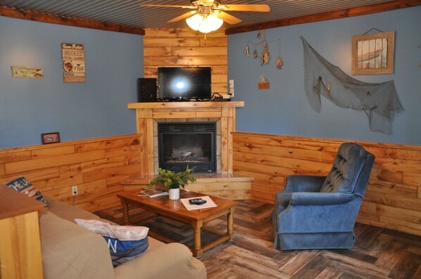 Una sala de estar acogedora con chimenea, paredes de madera, un televisor y un sillón azul.