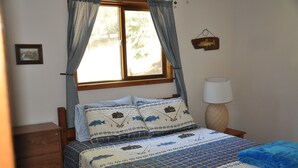 A bedroom with a bed, a nightstand, a lamp, and a window with curtains. - 01) The Fishing Lodge (Bayfield)