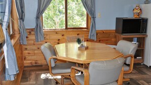 A cozy cabin-style room with a wooden dining table, four chairs, a small plant, and a television on a wooden stand. - 01) The Fishing Lodge (Bayfield)