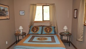 Ein Schlafzimmer mit einem großen Bett, zwei Nachttischen, einem Fenster mit Vorhängen und einem gerahmten Bild an der Wand.