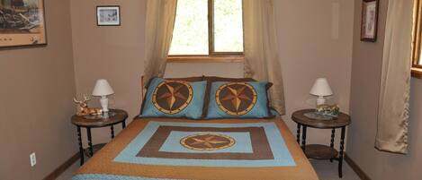 A bedroom with a large bed, two bedside tables, a window with curtains, and a framed picture on the wall.