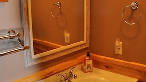 Ein Badezimmer mit einem Holzkosmetikschrank, einem weißen Waschbecken, einem Spiegel und einem Toilettenpapierhalter.