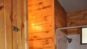 Un baño de madera con ducha, lavamanos y un perchero para toallas.