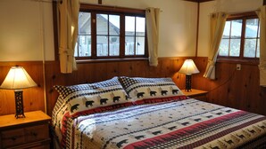 A cozy room with a large bed, wooden headboard, two bedside lamps, a wooden dresser, and windows with curtains. - 04) The Rustic Lodge (Bayfield)