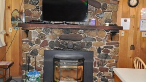 A stone fireplace with a television mounted above it, a clock on the wall, and a bag of wood pellets on the floor. - 04) The Rustic Lodge (Bayfield)