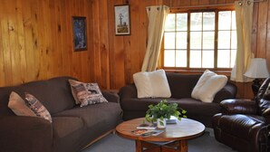 A cozy living room with a brown leather sofa, a wooden coffee table, and a window with curtains. - 04) The Rustic Lodge (Bayfield)