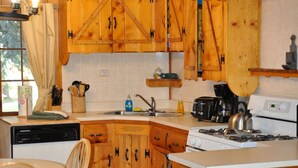 A compact kitchen with wooden cabinets, a gas stove, a dishwasher, and a dining area with a table and chairs. - 04) The Rustic Lodge (Bayfield)