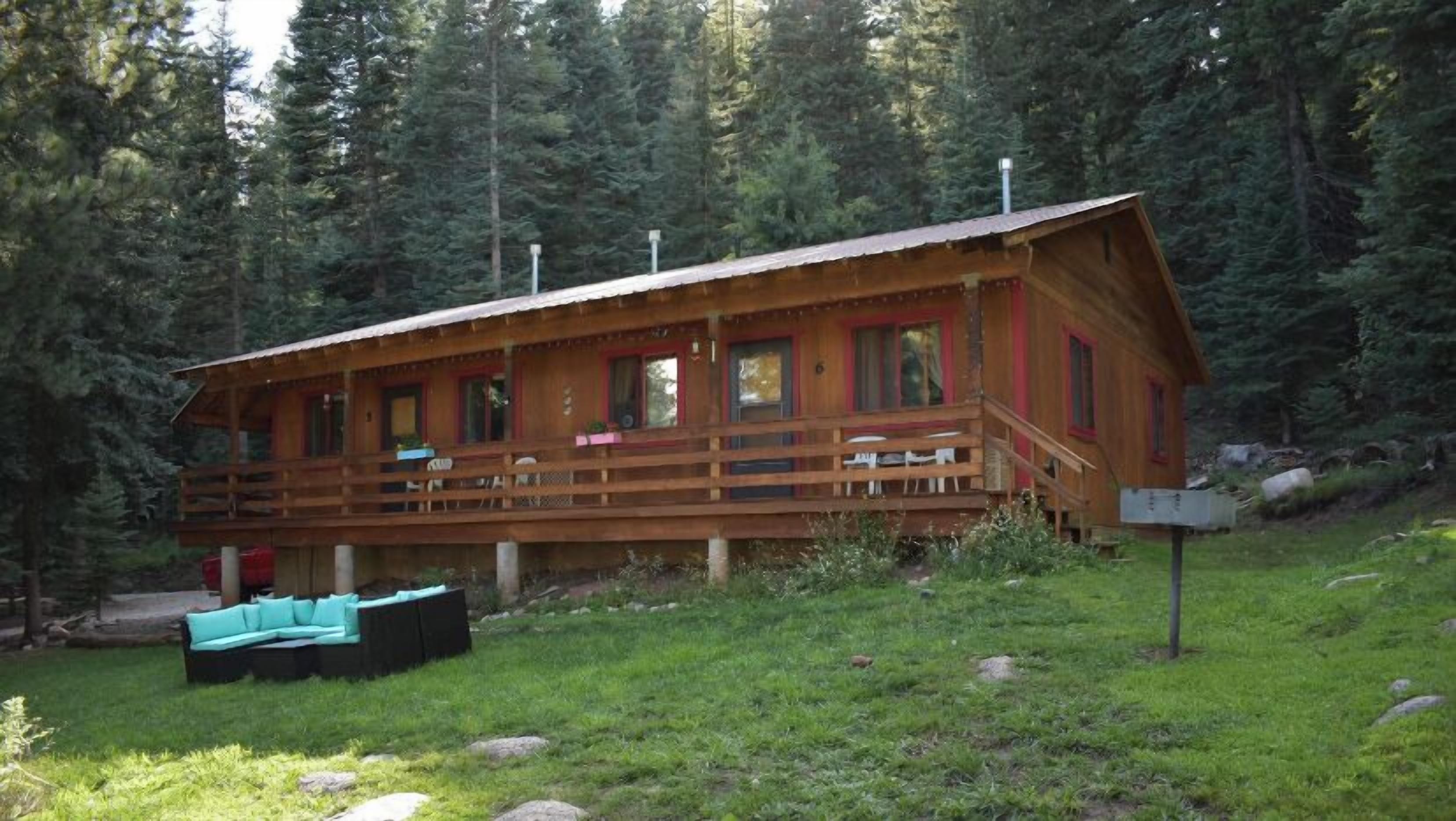 A cabin with a deck, surrounded by forest.