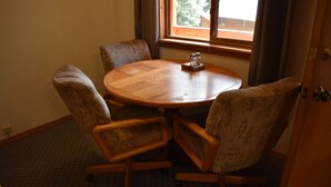 A round wooden table with four upholstered chairs, a window with curtains, and a door. - 0005) The Wolf Cabin (Bayfield)