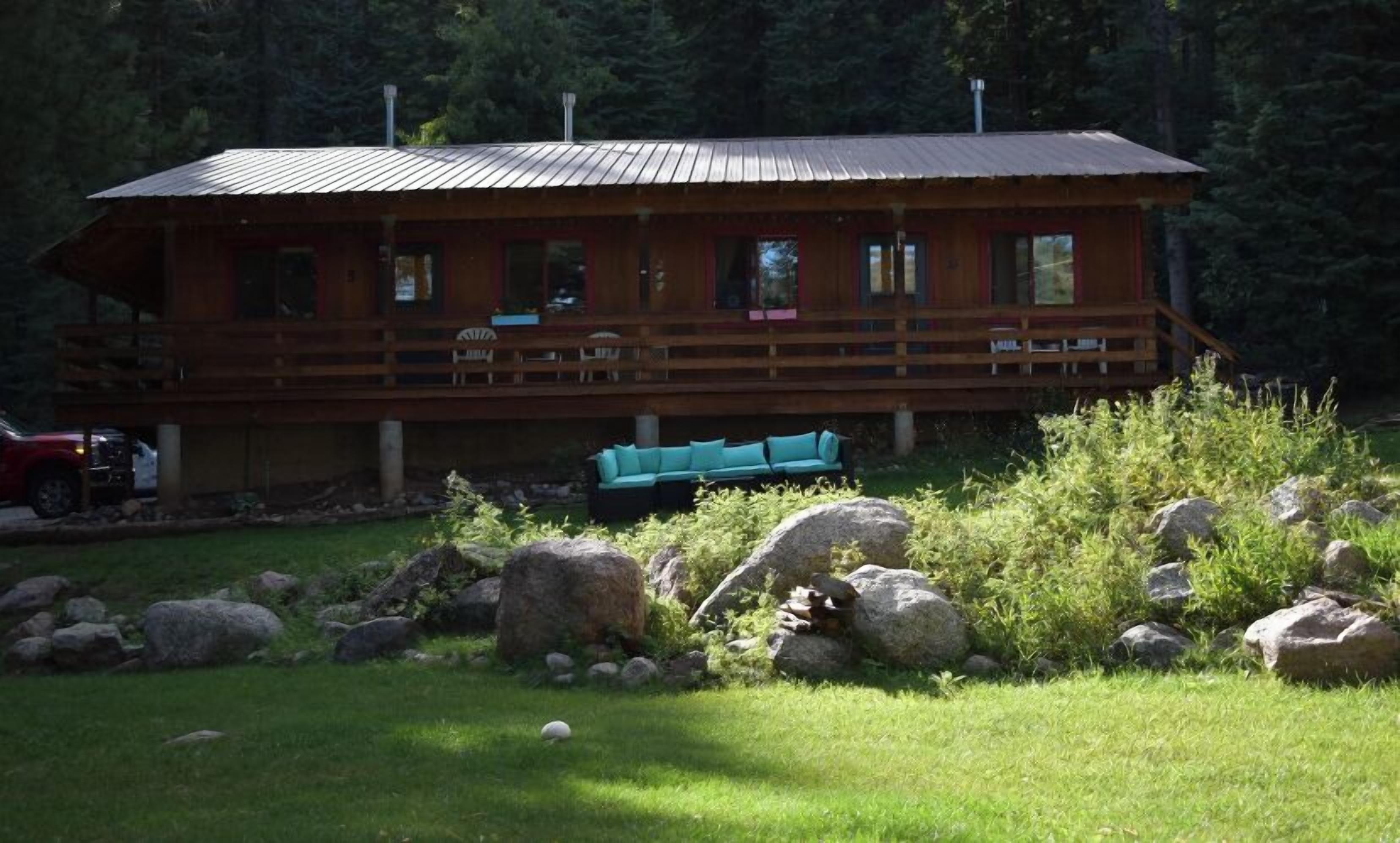 Een houten vakantiehuis met een veranda, omringd door rotsen en groen.