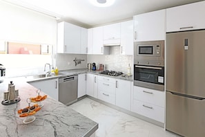 A modern kitchen with white cabinets, stainless steel appliances, and a marble countertop.