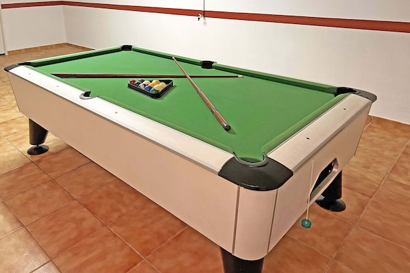 A pool table with a green felt surface, a cue stick, and a set of billiard balls.