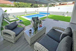 A covered patio with wicker furniture, a pool, and a well-maintained lawn.