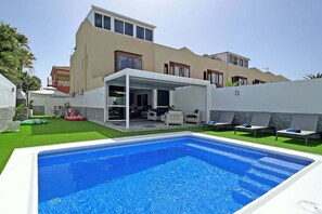 A modern house with a swimming pool, outdoor seating, and a covered patio.