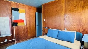 Um quarto com uma cama grande, paredes de painel de madeira, uma luminária no teto e uma porta.