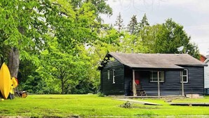 Uma cabana rústica com varanda, rodeada por vegetação exuberante e um lago.