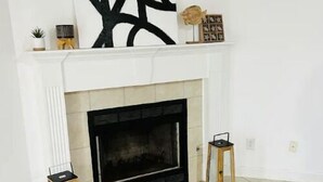 Una sala de estar moderna con chimenea, un cuadro abstracto grande sobre ella y dos mesitas.
