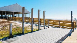 Una pasarela de madera que conduce a un espacio cubierto con techo de metal, probablemente una instalación junto a la playa.