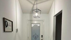 Un pasillo con suelo de madera, una puerta blanca con panel de vidrio decorativo y una lámpara colgante.
