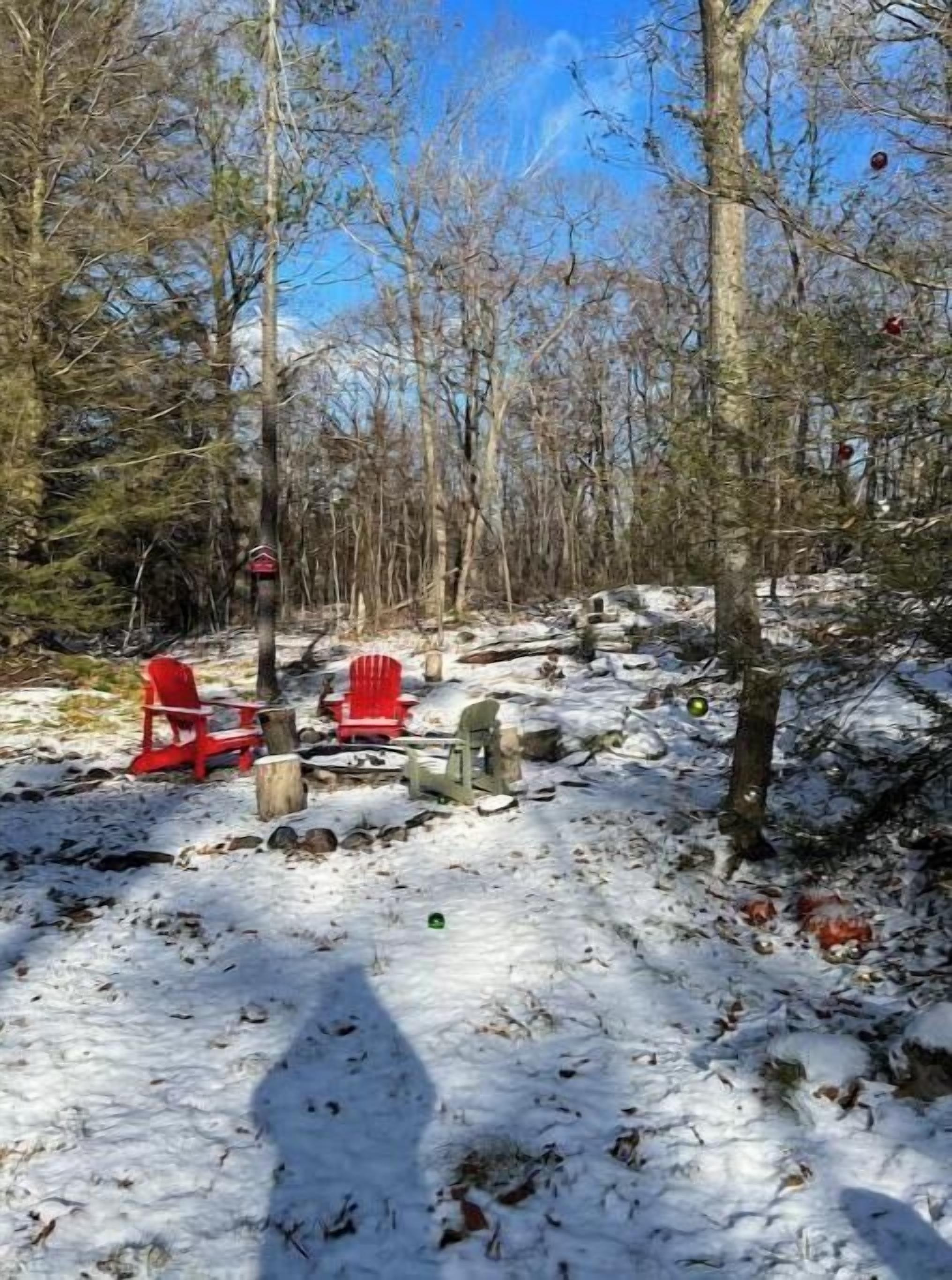 Ett snötäckt utomhusområde med två röda Adirondack-stolar och en eldstad.