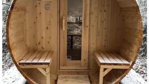 Lumisen metsän keskelle rakennettu puinen sauna, jossa on kaksi penkkiä ja ovi.