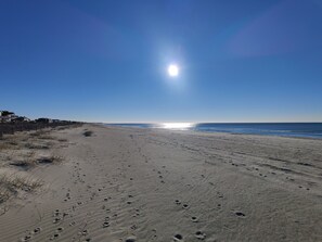 A beach with footprints leading to the water, a clear sky, and houses in the background. - Sandy Snouts Retreat, Pet Friendly Home With Fire Pit in Holden Beach, NC (Holden Beach)