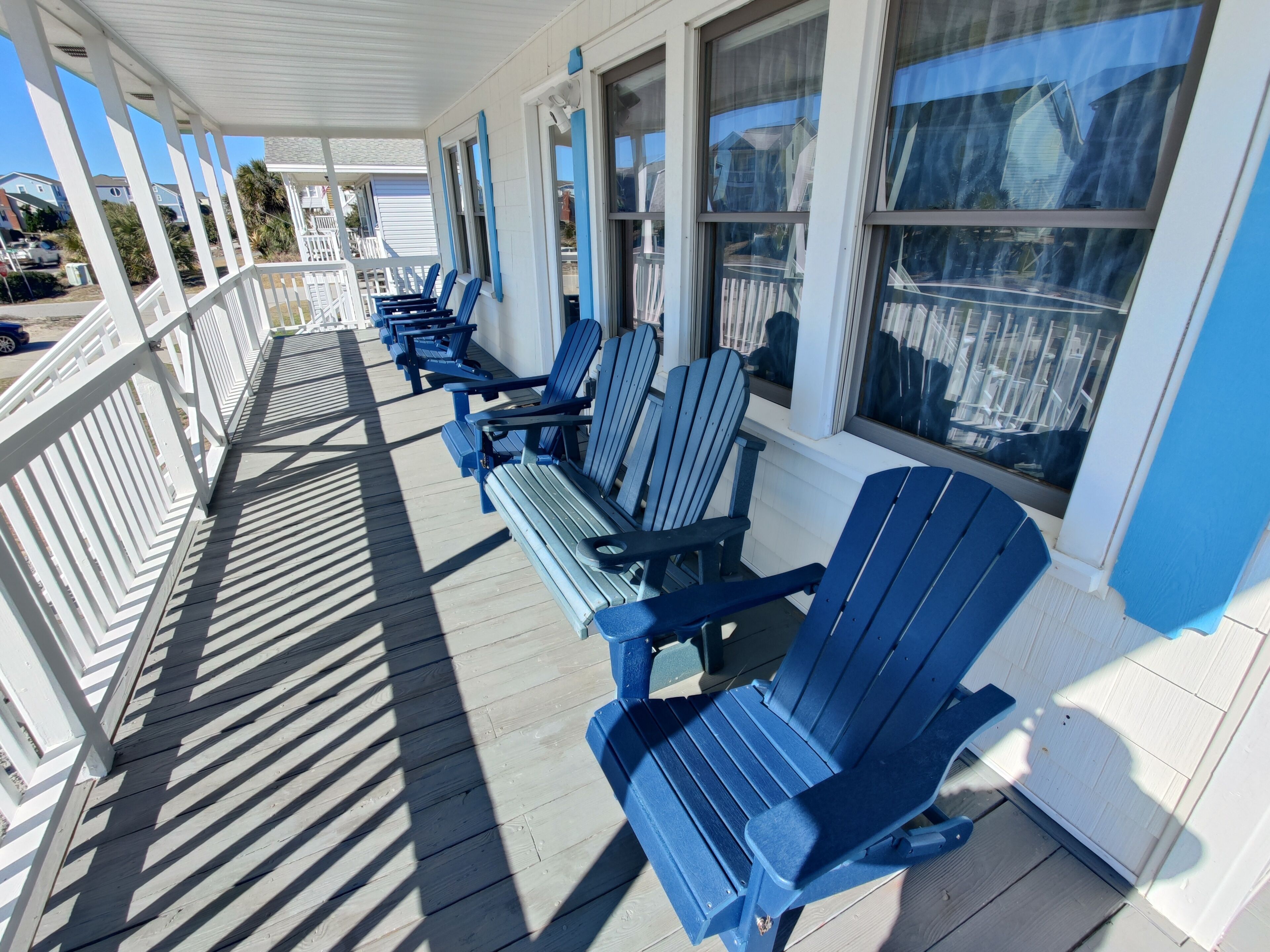 A covered outdoor seating area with blue Adirondack chairs and white railings.