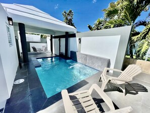 A swimming pool with a tiled deck, lounge chairs, and a covered seating area.