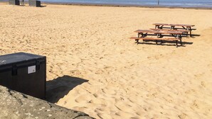 Een zanderig strand met picknicktafels en een zwarte tas.