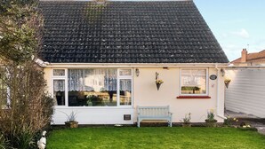 Een gelijkvloers huis met een pannendak, een veranda met een bankje en een kleine tuin.