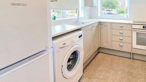 Een keuken met een wasmachine, een spoelbak, kasten en een raam.
