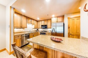A modern kitchen with wooden cabinets, stainless steel appliances, and a granite countertop. - 2 Bedroom Ski-in, Ski-out Condo at The Timbers (Keystone)
