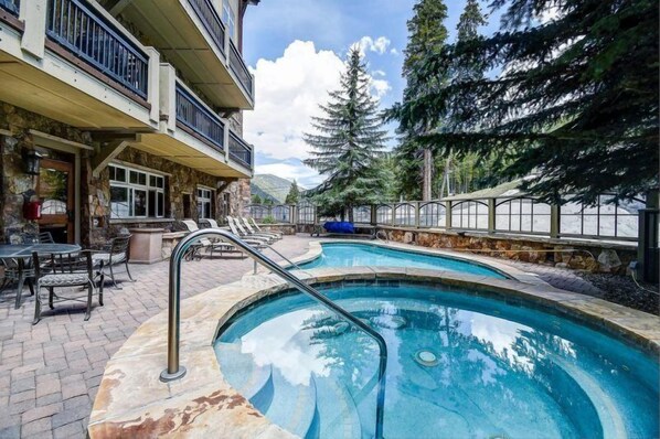 A pool area with a stone deck, lounge chairs, and a view of trees and mountains.