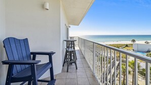 Un balcon avec deux fauteuils Adirondack, une petite table et une vue sur la plage et l’océan.