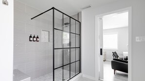 Ein modernes Badezimmer mit Duschkabine aus Glas, weißen Fliesen und einer sichtbaren Dusche.