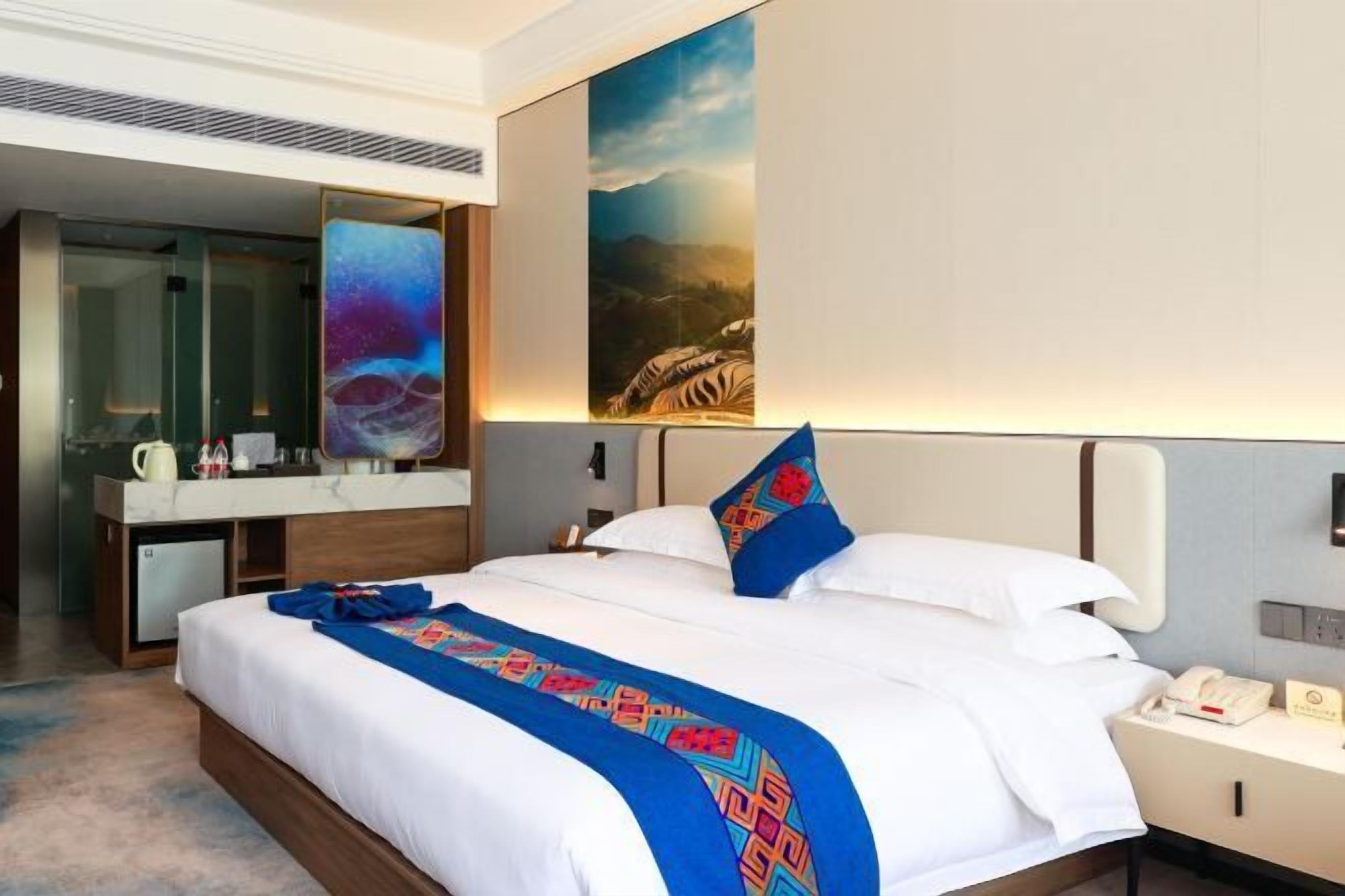 A hotel room with a large bed, a desk, a mirror, and a painting on the wall.